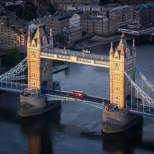 Aerial view of London’s Tower Bridge at sunset with a red double-decker bus crossing over the River Thames.